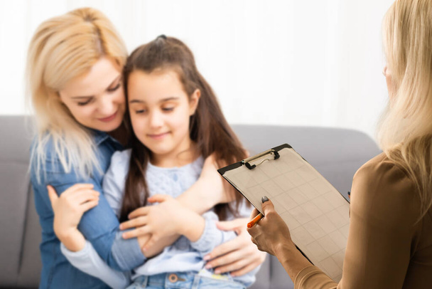 Ręka profesjonalnego psychoterapeuty rodzinnego piszącego notatki przed rodziną z dzieckiem podczas konsultacji. - Zdjęcie, obraz