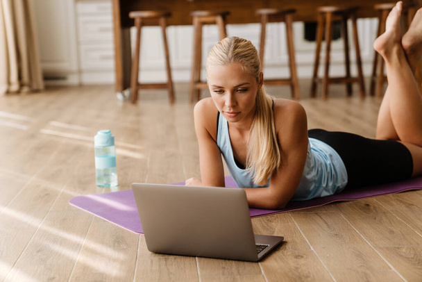 Blonde young woman using laptop during yoga practice at home - Photo, image