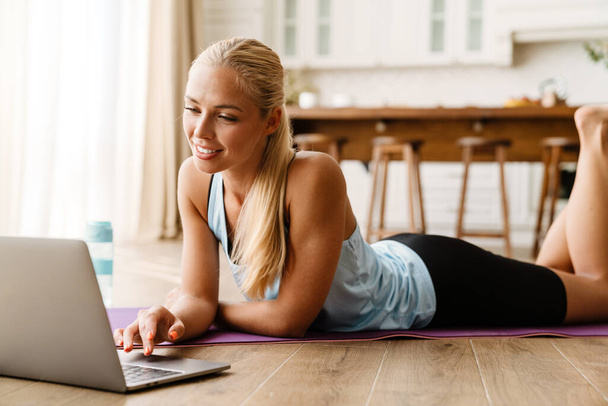 Blonde young woman using laptop during yoga practice at home - Fotó, kép