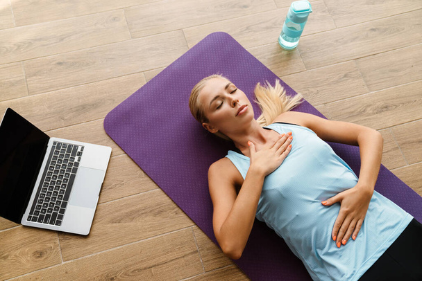 Blonde young woman doing breathing exercise during yoga practice at home - Zdjęcie, obraz