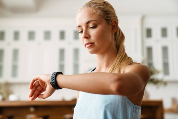 Blondynka młoda kobieta za pomocą smartwatch podczas treningu w domu - Zdjęcie, obraz
