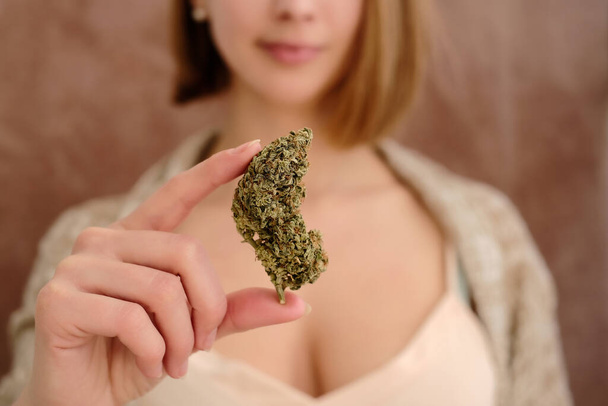 Primer plano del brote de cannabis en la mano de una joven sobre un fondo marrón. Concepto de uso médico de marihuana. - Foto, imagen
