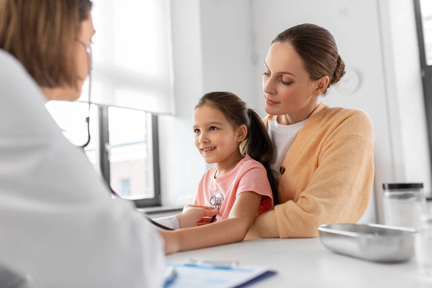 medicine, healthcare and pediatry concept - mother with little daughter and doctor with stethoscope at clinic - Photo, image