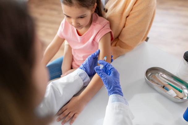 medicine, healthcare and pediatry concept - female doctor or pediatrician with syringe making vaccine injection to little girl patient at clinic - Zdjęcie, obraz