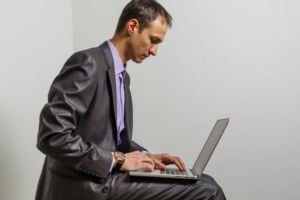 Positive young man using laptop computer over grey studio background. - Foto, Imagen
