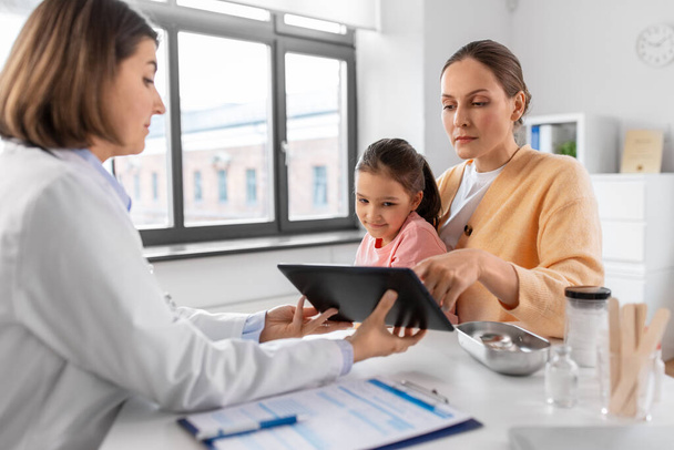 medicine, healthcare and pediatry concept - mother with little daughter and doctor showing tablet pc computer at clinic - Foto, Bild