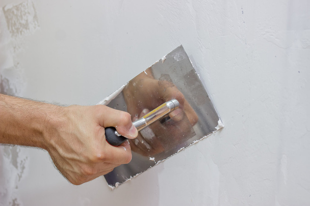 Мужская рука с лопаткой, оштукатуривающей стену
 - Фото, изображение