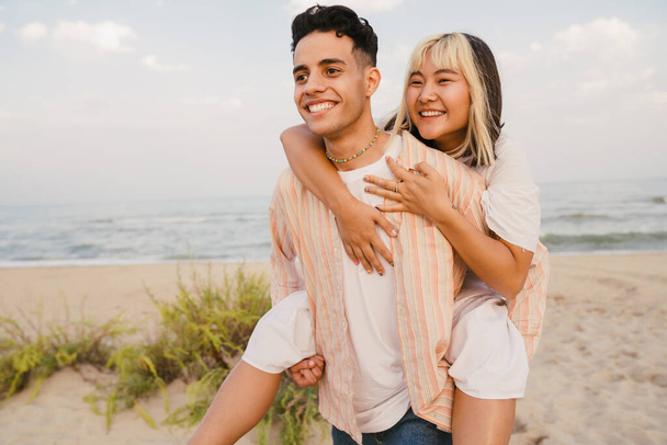 Multiracial young couple smiling while piggybacking on summer beach - Fotografie, Obrázek