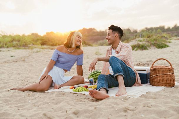 Monirotuinen pari hymyilee ja puhuu piknikillä kesärannalla - Valokuva, kuva