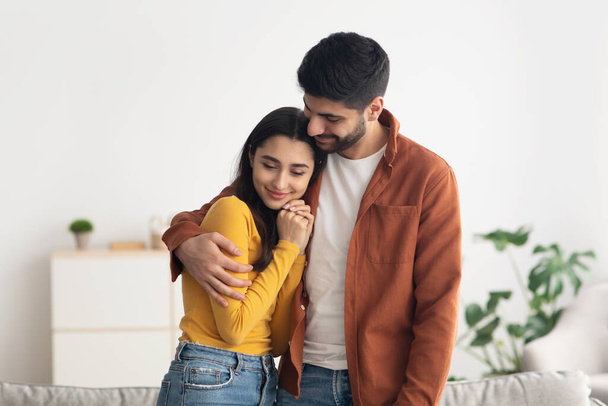 Happy Middle Eastern Couple Embracing Standing At Home. Young Arabic Husband Hugging His Beautiful Wife Indoor. Love And Romantic Relationship. Successful Marriage Concept - Fotografie, Obrázek