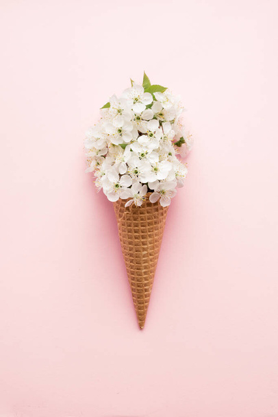 薄ピンク色のパステルカラーの背景に白い桜の花とワッフル甘いアイスクリームコーンのフラットレイ。春のムードを最小限の概念。トップ表示. - 写真・画像