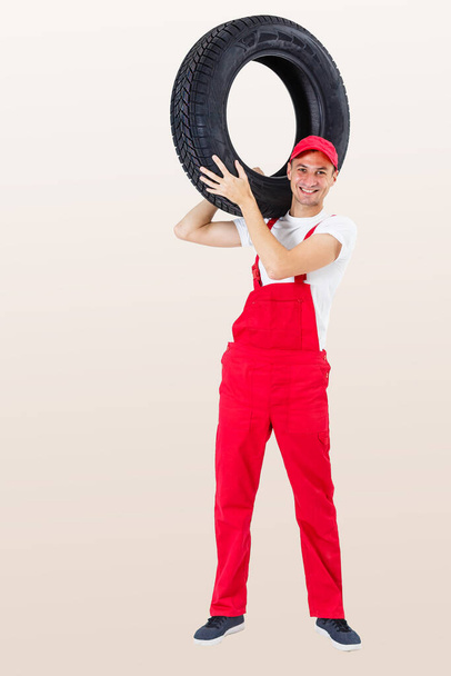Рабочий мужчина в полном росте держит шину на белом фоне - Фото, изображение