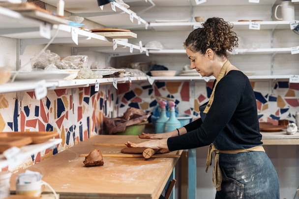Stock photo of happy woman in apron working in pottery atelier and using clay. - Foto, Imagem