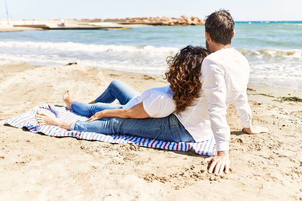 Casal hispânico de meia idade relaxado sentado na toalha na praia. - Foto, Imagem