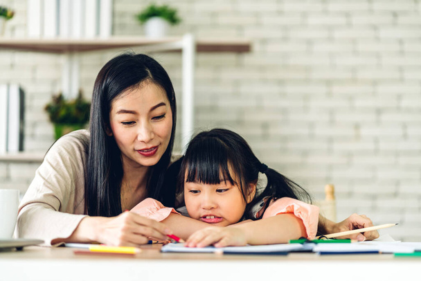 Портрет щасливої любові азіатської сім'ї мати вчить маленьку дочку азіатську дівчинку вчитися і вчитися на столі. Мама і азіатська молода дівчина пишуть з книгою і олівцем уроки вдома. Освіта
 - Фото, зображення