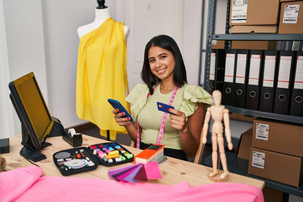 Trabajadora de negocios de comercio electrónico de mujer latina joven usando teléfono inteligente y tarjeta de crédito en el estudio de diseño - Foto, imagen