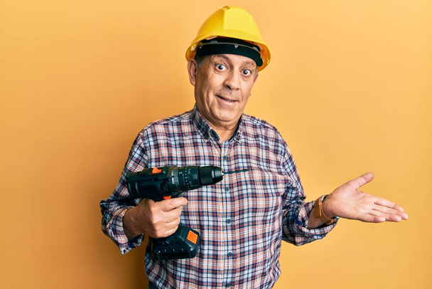 Handsome senior man with grey hair holding screwdriver wearing hardhat celebrating achievement with happy smile and winner expression with raised hand  - Photo, Image