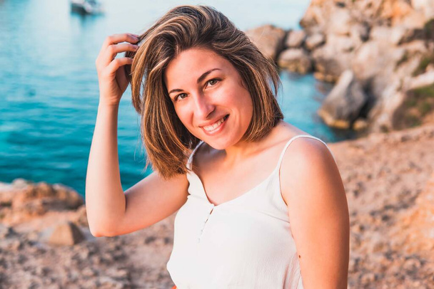 Портрет, улыбающаяся молодая женщина в отпуске, выдергивающая волосы из воздуха, в бухте Портал Веллс, остров Пальма де Майорка, Испания. - Фото, изображение