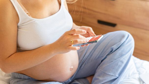 Εφαρμογή για την υγεία εγκυμοσύνης. Έγκυος γυναίκα κρατώντας smartphone. Κινητή εγκυμοσύνη σε απευθείας σύνδεση εφαρμογή μητρότητας. Έννοια της εγκυμοσύνης, μητρότητας, προσδοκία για τη γέννηση του μωρού - Φωτογραφία, εικόνα