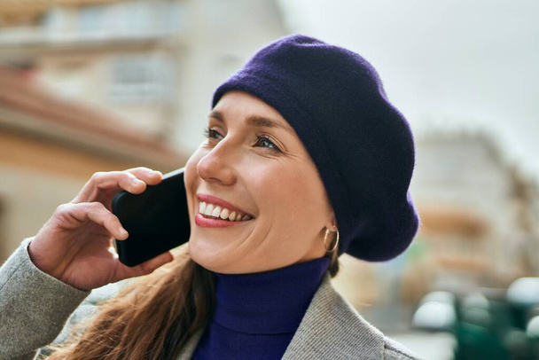 Mujer rubia joven sonriendo feliz hablando en el teléfono inteligente en la ciudad. - Foto, imagen