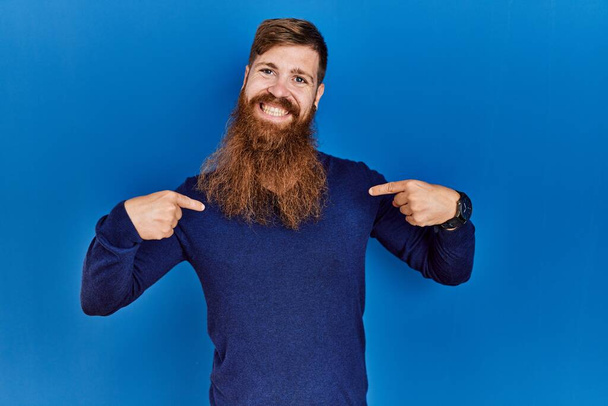Redhead man with long beard wearing casual blue sweater over blue background looking confident with smile on face, pointing oneself with fingers proud and happy.  - Foto, imagen