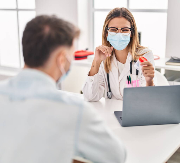 Fiatal férfi és nő orvos és beteg orvosi maszkot visel vizelet kémcsővel a klinikán - Fotó, kép