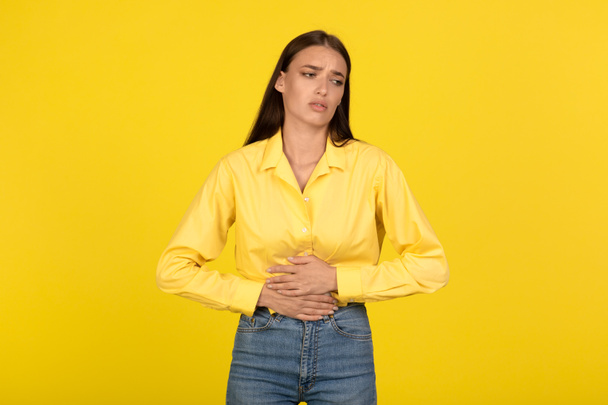 Unhappy Young Female Suffering From Stomachache Touching Aching Abdomen Standing On Yellow Studio Background. Abdominal Pain, Gastritis Health Problems Concept - Photo, Image