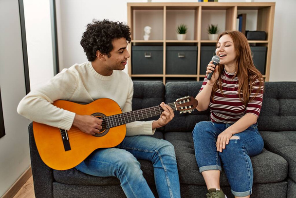 Молодая пара играет на классической гитаре и поет дома с помощью микрофона. - Фото, изображение