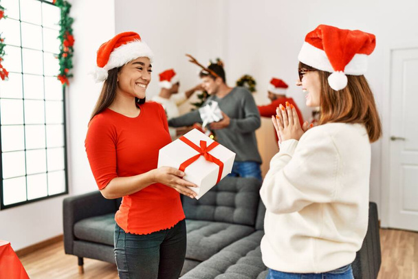 Groupe de jeunes à la réunion de Noël. Femme surprenante avec un cadeau à une autre fille à la maison. - Photo, image
