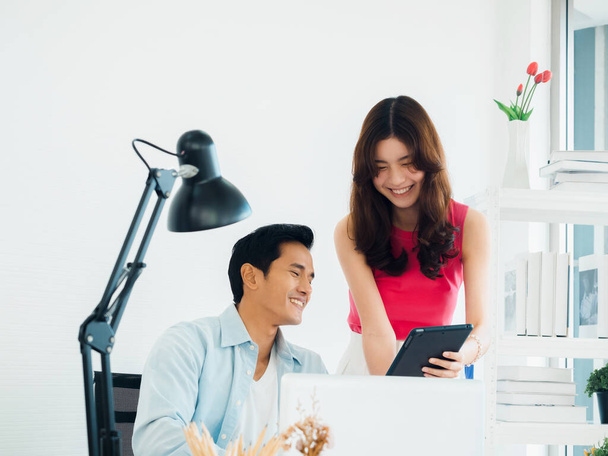 Šťastný usměvavý asijský obchodní pár, mladý muž a žena, kolegové pomocí tabletu a notebooku na stole, při pohledu na obrazovku, pracuje společně na bílém čistém malém kancelářském pozadí. - Fotografie, Obrázek