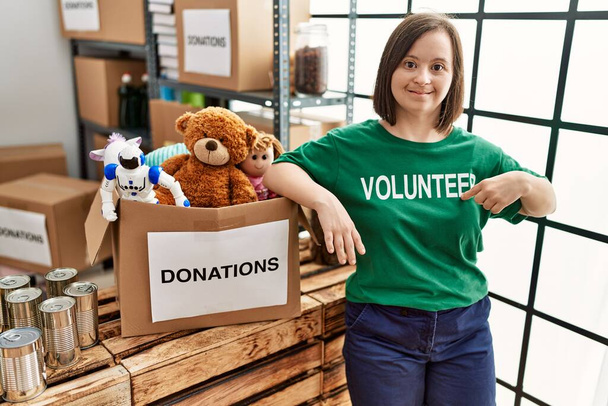 Femme brune avec le syndrome du duvet debout par boîte avec des jouets donnés au stand de dons - Photo, image