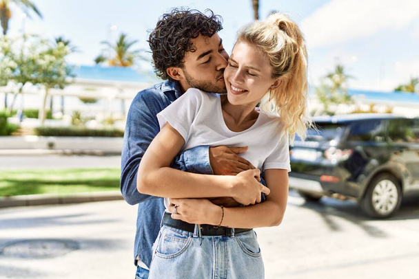 Young beautiful couple of caucasian girlfriend and hispanic boyfriend hugging in love outdoors on a sunny day. Woman and man smiling happy dating relationship - Φωτογραφία, εικόνα