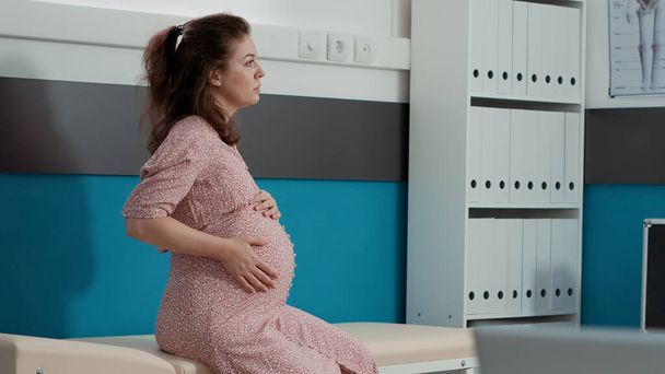 妊娠中のお腹を持つ女性の肖像は、健康専門家との相談予約を開始するのを待っています.将来の母親は子供を期待し、医療キャビネットの検査に出席する. - 写真・画像