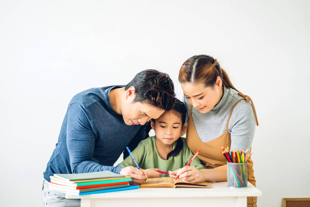 Мама и папа с маленькой девочкой, пишущей с книгой, делают домашнее задание в домашней школе на дому. - Фото, изображение
