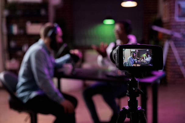 Multiethnic team of people meeting to broadcast internet podcast, recording video discussion on camera. Influencer and guest talking on online livestream to create social media channel content. - Foto, Imagen
