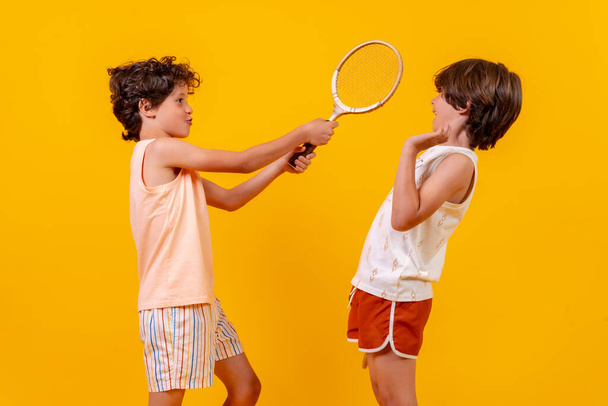 Two brothers playing tennis and having fun on summer vacation, yellow background - 写真・画像