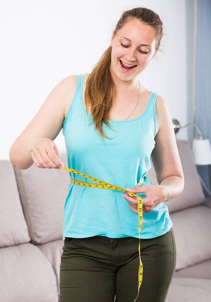 Young woman feeling happy measuring her waist at home - Фото, зображення