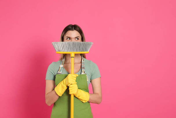 Young woman with yellow broom on pink background, space for text - Фото, изображение