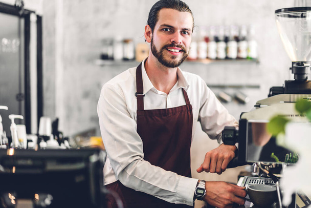 Retrato de sonrisa guapo barbudo barista hombre puesta en marcha dueño de una pequeña empresa que trabaja y mira la cámara recibir orden del cliente detrás de la barra de mostrador en un café - Foto, imagen