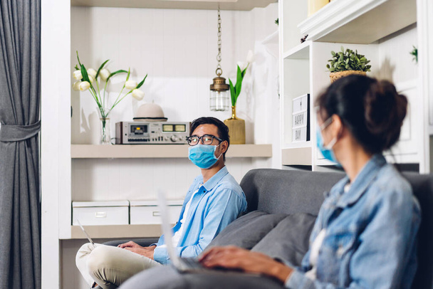 Νεαρό ασιατικό ζευγάρι που χρησιμοποιεί φορητό υπολογιστή εργασίας και τηλεδιάσκεψης συνάντηση σε απευθείας σύνδεση συνομιλία σε καραντίνα για coronavirus φορώντας προστατευτική μάσκα με κοινωνική απόσταση στο σπίτι.work από το σπίτι έννοια - Φωτογραφία, εικόνα