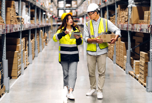 Asian two engineer team shipping order detail on tablet check goods and supplies on shelves with goods background inventory in factory warehouse.logistic industry and business export - Photo, Image