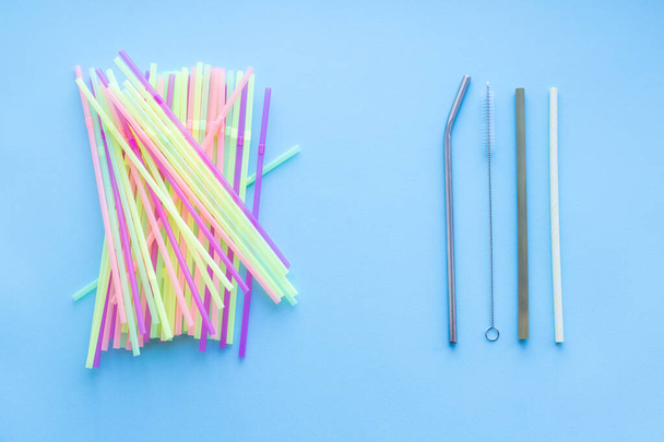 Many plastic drinking straws vs one reusable metal or bamboo drinking straw and cleaning brush on a blue background. Zero waste sustainable living, plasticfree concept. Eco friendly plastic free items - Photo, Image