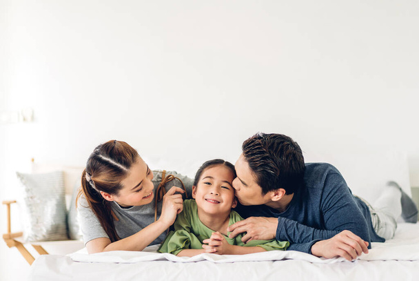 Portré élvezze boldog mosolygós szeretet ázsiai család apa és anya fiatal szülőkkel kicsi gyermek ázsiai lány lánya játszani, és keres együtt pillanatok alatt jó időt feküdt az ágyon otthon - Fotó, kép