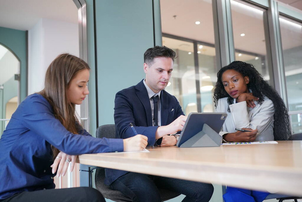 Image de jeunes hommes d'affaires et collègues discutant du document dans un ordinateur portable et un pavé tactile lors d'une réunion - Photo, image