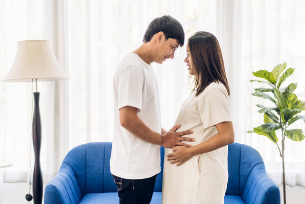 Romantic sweet asian couple husband hugging and smiling beauty asian pregnant wife.Man expecting with woman pregnancy hold to baby in belly at home - Fotoğraf, Görsel