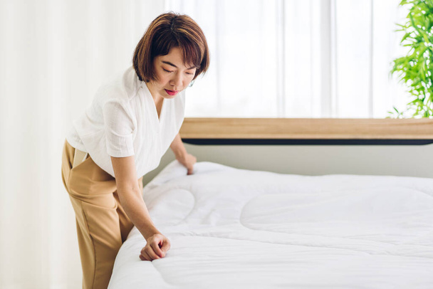 若いアジアの女性の主婦は、ベッドをきれいにし、ベッドルームをきれいに白いクリーンなシートでベッドシートを変更設定します。 - 写真・画像