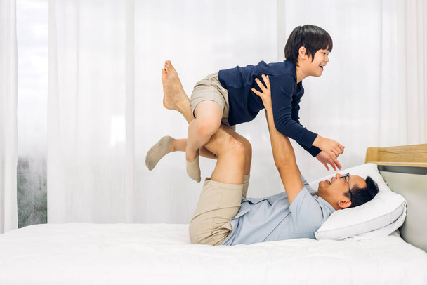 Портрет щасливого кохання азіатського батька сім'ї, що носить маленького азіатського хлопчика, який посміхається грати в супергероя і весело провести час в ліжку вдома
 - Фото, зображення