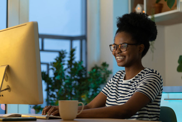 Szczęśliwa uśmiechnięta projektantka lubi pracować w domu nad nowym zdalnym projektem. Udany afrykański programista kodujący nowy program, stronę internetową lub oprogramowanie. młody freelance czarny kobieta na odległość okupacja - Zdjęcie, obraz