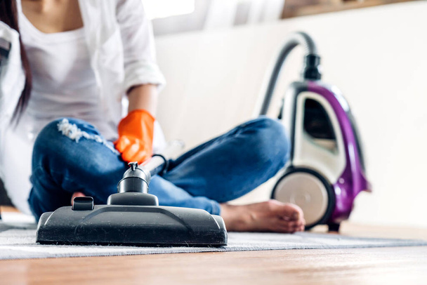 Giovane donna in guanti protettivi pulizia casa con aspirapolvere in soggiorno a casa
 - Foto, immagini