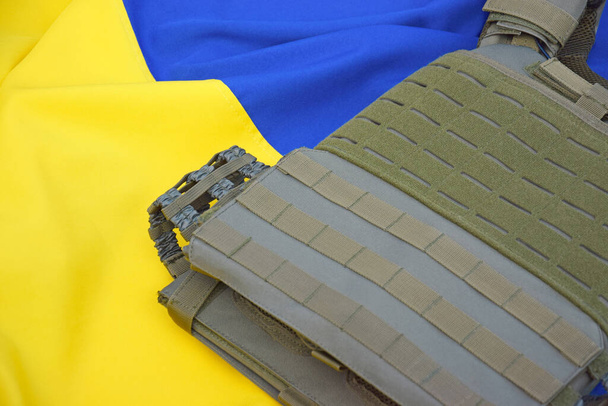 Τακτική, στρατιωτική πανοπλία με πλάκες στο φόντο της σημαίας της Ουκρανίας. Η έννοια της προστασίας του σώματος από πυροβολισμούς στον πόλεμο στην Ουκρανία. - Φωτογραφία, εικόνα